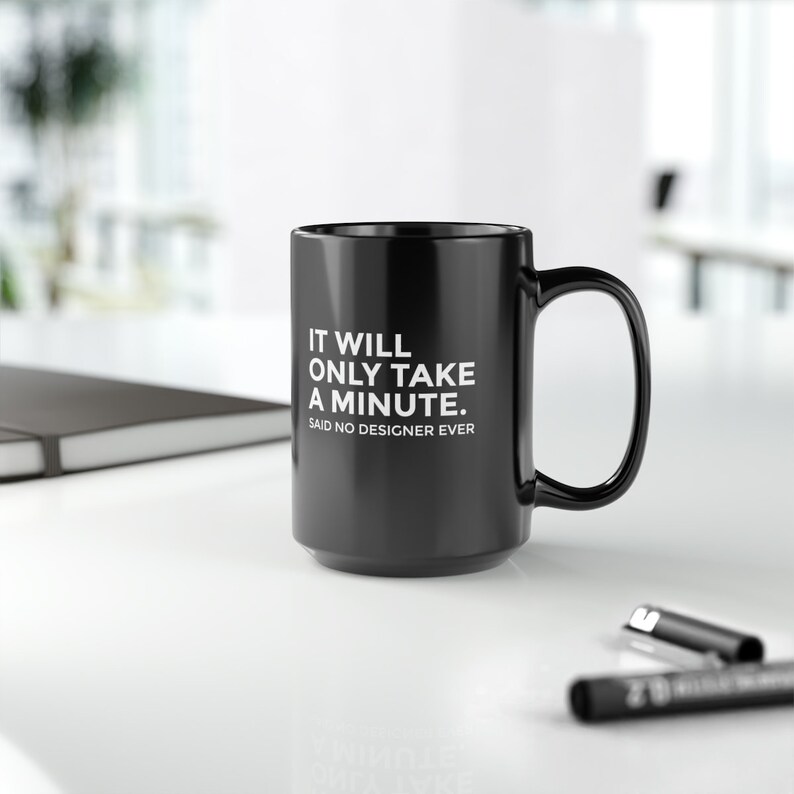 K&ouml;nnte beinhalten: Schwarze Keramik-Tasse mit gro&szlig;em Henkel. Die Tasse hat einen wei&szlig;en Text mit der Aufschrift: "IT WILL ONLY TAKE A MINUTE. SAID NO DESIGNER EVER."