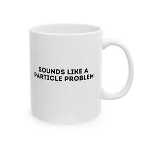 Puede incluir: Taza de cerámica blanca con asa curvada. La taza presenta la frase "SOUNDS LIKE A PARTICLE PROBLEM" impresa en negro. Ideal para bebidas calientes, perfecta para el hogar o la oficina.
