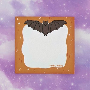 May include: A square sticky note with a brown border featuring a central white area for writing. A dark brown bat illustration is positioned at the top center. The border includes small white stars and orange dashes. The text hello, Hollory is printed.