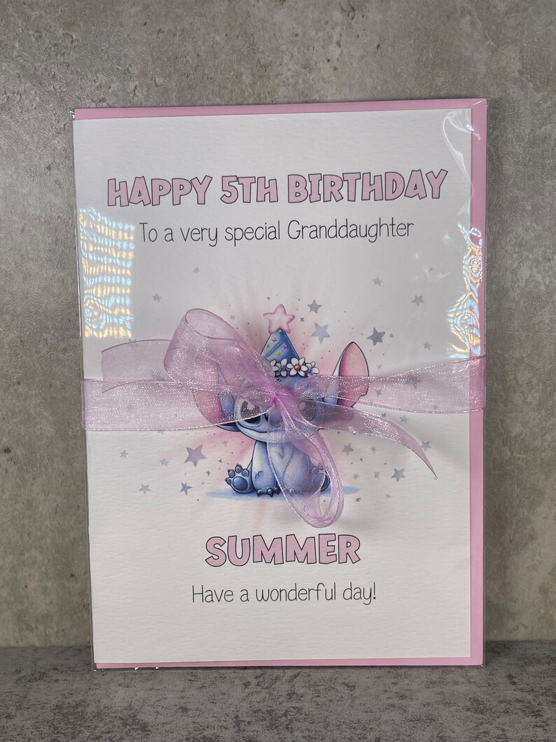 May include: A pink birthday card with a blue cartoon character wearing a party hat. The card says "Happy 5th Birthday" and "To a very special Granddaughter". The character's name is "Summer" and the card says "Have a wonderful day!"