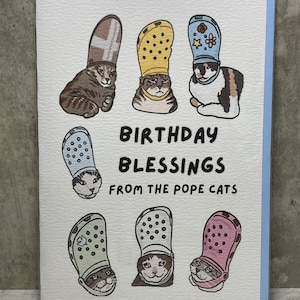 Puede incluir: Una tarjeta de felicitaci&oacute;n con una ilustraci&oacute;n humor&iacute;stica de gatos que llevan diferentes estilos de zapatos Crocs como sombreros. El texto dice "Birthday Blessings from the Pope Cats".