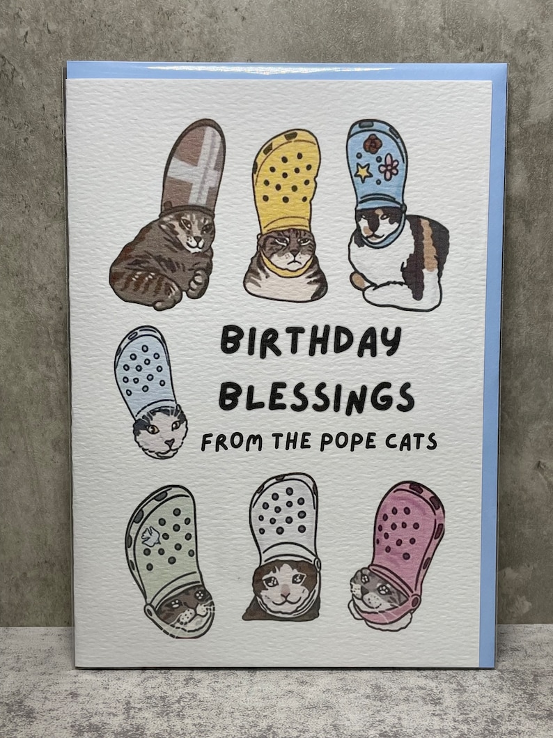 Puede incluir: Una tarjeta de felicitaci&oacute;n con una ilustraci&oacute;n humor&iacute;stica de gatos que llevan diferentes estilos de zapatos Crocs como sombreros. El texto dice "Birthday Blessings from the Pope Cats".