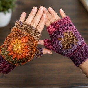 May include: A pair of fingerless crochet gloves featuring a central floral motif. The left glove displays warm tones of orange, yellow, and brown, while the right glove showcases shades of purple, magenta, and brown. Both have ribbed cuffs.