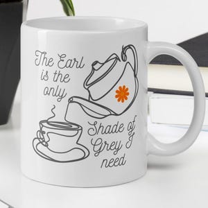 Puede incluir: Taza de cerámica blanca con una ilustración en negro y naranja de una tetera vertiendo té en una taza. El texto en la taza dice "The Earl is the only Shade of Grey I need."