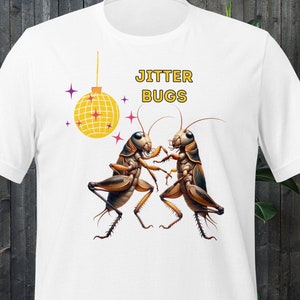 May include: White t-shirt featuring a graphic of two brown crickets dancing in front of a yellow disco ball with the text "Jitter Bugs" above them.