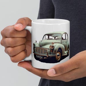 May include: White ceramic mug featuring an illustration of a green vintage car and the word "Tobbe" printed on the front.