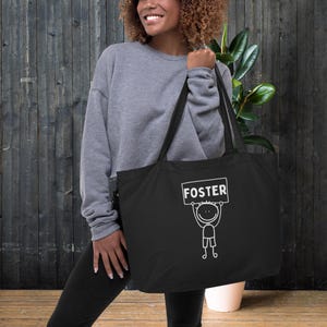 May include: Black tote bag with a white stick figure holding a sign that says "FOSTER".