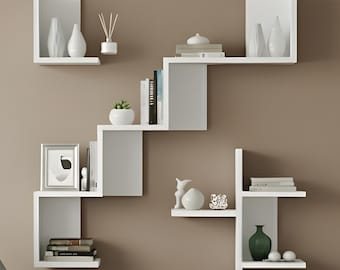 May include: A modern living room scene featuring a gray armchair with wooden legs, a dark brown coffee table, and a series of white floating shelves on a brown wall. The shelves display decorative items like vases, books, and a small plant, creating a minimalist aesthetic.