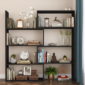 May include: A black bookcase displaying books, decorative plates, vases, and small sculptures. The shelves are arranged with a variety of items, including a small mirror, an hourglass, and a Buddha statue. The overall aesthetic is modern and organised.