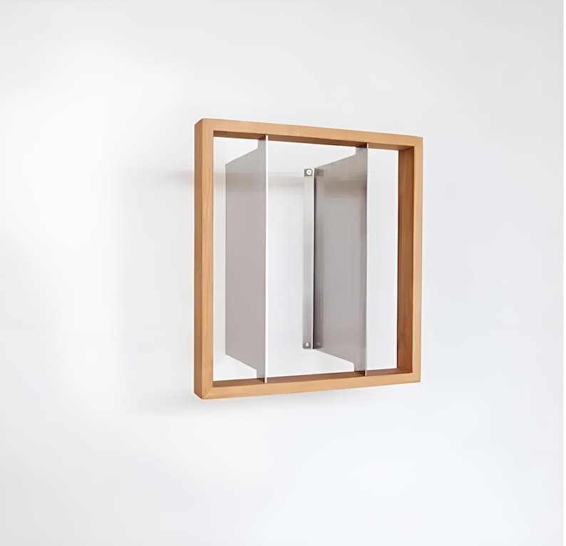 May include: A modern wall art piece featuring a light brown wooden frame with three vertical, rectangular, silver-colored panels. The panels are arranged within the frame, creating a minimalist, geometric design. The artwork is mounted on a white wall.