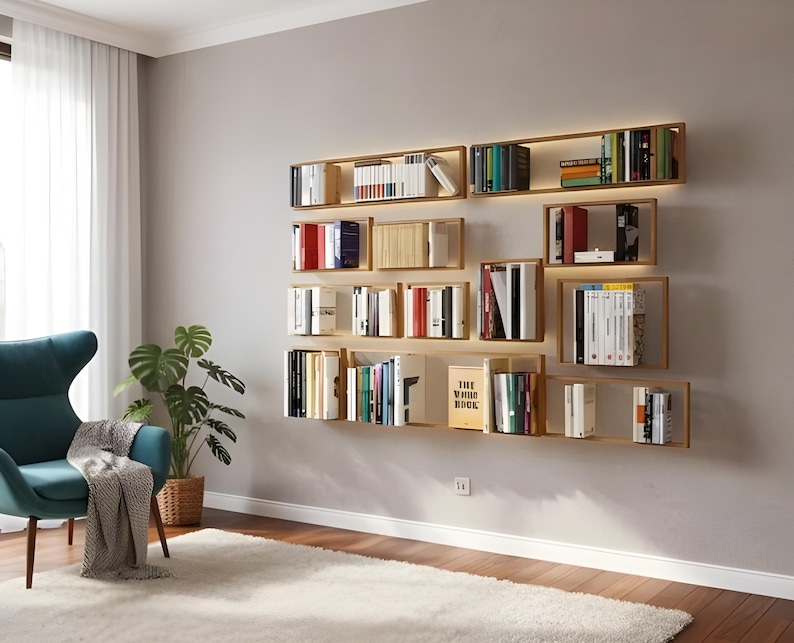 May include: A modern living room with a wall-mounted bookshelf system. The shelves are made of light wood and are filled with books of various sizes and colors. The room also features a teal armchair, a potted plant, and a fluffy white rug.