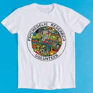 May include: White t-shirt with a circular graphic design featuring the text "Psychedelic Research Volunteer" and a colorful illustration of psychedelic imagery, including mushrooms, aliens, and a skull.