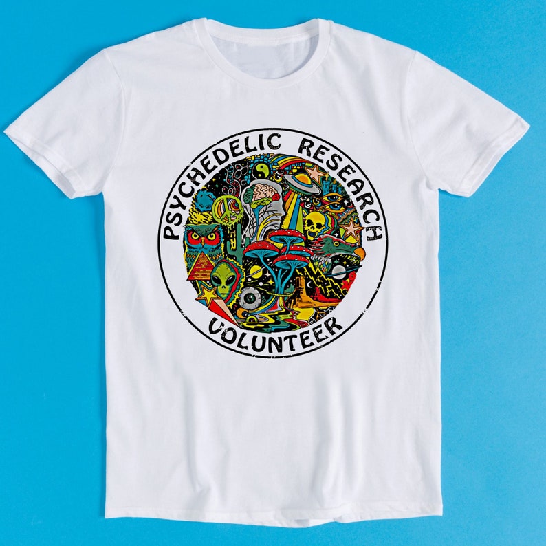 May include: White t-shirt with a circular graphic design featuring the text "Psychedelic Research Volunteer" and a colorful illustration of psychedelic imagery, including mushrooms, aliens, and a skull.