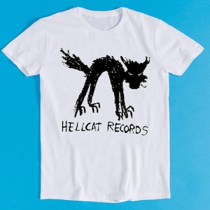 May include: White t-shirt with a black and white illustration of a cat and the text "Hellcat Records".