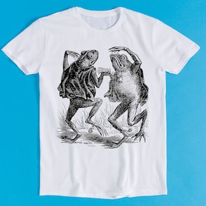 May include: A white t-shirt with a black and white illustration of two frogs dancing. The frogs are wearing cloaks and have large eyes.