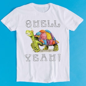 May include: White t-shirt featuring a colorful turtle illustration with the words "SHELL YEAH!" in black. The turtle has a multi-colored shell and is wearing a party hat. The shirt is made of a soft, comfortable material.