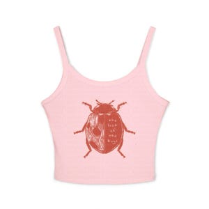 May include: A light pink ribbed crop top with thin spaghetti straps. The centre features a red graphic illustration of a ladybug with the text "the last of the bugs" printed on the right side of the insect's wing in a simple, handwritten font.