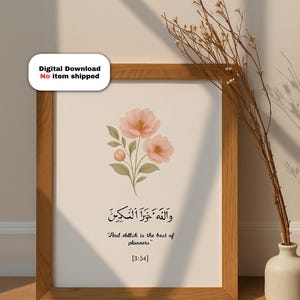 Puede incluir: Una impresión artística enmarcada con flores de acuarela en tonos rosa y verde. La impresión incluye caligrafía árabe y la frase en inglés "And Allah is the best of planners". El marco es de madera.