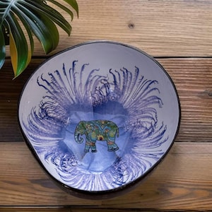 May include: A white ceramic bowl with a blue and purple design. The bowl features a stylised elephant with intricate patterns in the centre. The bowl is perfect for serving snacks or salads.