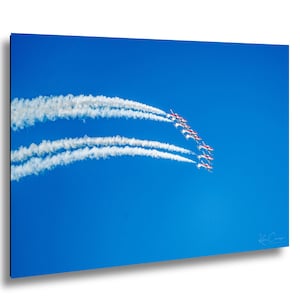 May include: A photograph showing a formation of red and white aeroplanes against a clear blue sky. The aircraft are leaving white vapour trails, forming a curved pattern. A vibrant display of aerial acrobatics.