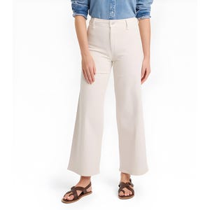 May include: Cream-colored wide-leg pants. The pants have a high waist and a flared leg. The model is wearing brown sandals. The pants are made of a smooth, solid fabric. The pants are a neutral color.