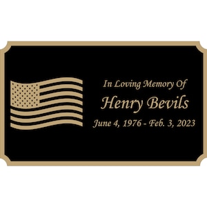 May include: A black memorial plaque with a gold border and a gold American flag. The text reads "In Loving Memory Of Henry Bevils June 4, 1976 - Feb. 3, 2023".