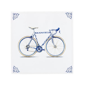Puede incluir: Una bicicleta de carretera azul y blanca con un patrón floral, sobre un fondo blanco. La bicicleta tiene neumáticos color canela, un asiento blanco y manillar azul. Diseños florales azules decorativos en las esquinas.