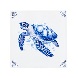Può includere: Una piastrella di ceramica blu e bianca con un'illustrazione dettagliata di una tartaruga marina che nuota. La tartaruga ha un guscio blu con segni bianchi ed è circondata da piccole farfalle blu.