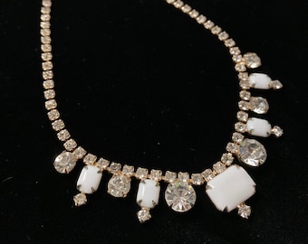 Op de afbeelding: Een gouden ketting met een rij heldere strass steentjes en een hanger met vijf witte rechthoekige stenen en heldere strass steentjes.