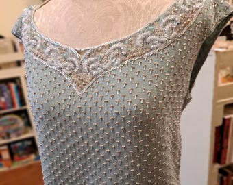 Op de afbeelding: Een lichtblauwe mouwloze top met een V-hals, versierd met ingewikkeld kralenwerk langs de halslijn en over het hele kledingstuk. De top wordt getoond op een mannequin, waarbij de textuur en het gedetailleerde ontwerp worden benadrukt.