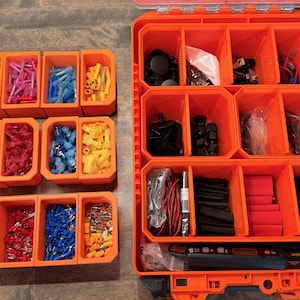 May include: A large orange plastic storage case with multiple internal compartments containing various electrical components, including wire connectors, heat shrink tubing, and a digital multimeter, alongside several smaller orange bins.