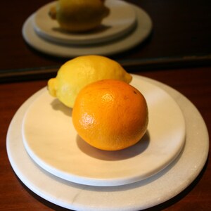 Puede incluir: Dos piezas de fruta, un limón amarillo y una naranja, están en un plato blanco. El plato está en un plato blanco más grande, que está sobre una superficie de madera.