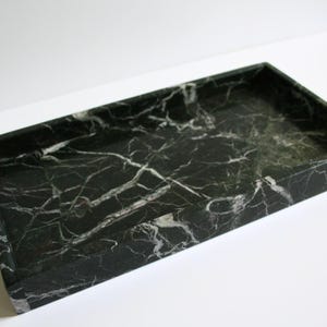 May include: A black marble tray with white veining. The tray is rectangular and has a smooth surface.