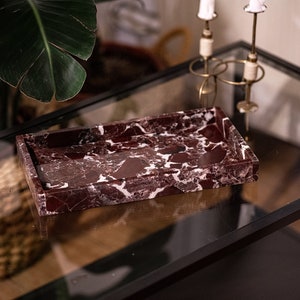 May include: A rectangular marble tray with a red and white marbled pattern. The tray is sitting on a glass table with a black frame.