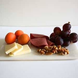 Könnte beinhalten: Ein weißes Marmor-Servierbrett mit einer Auswahl an Snacks, darunter geschnittener Käse, rotes Fleisch, Trauben, Walnüsse und Aprikosen.