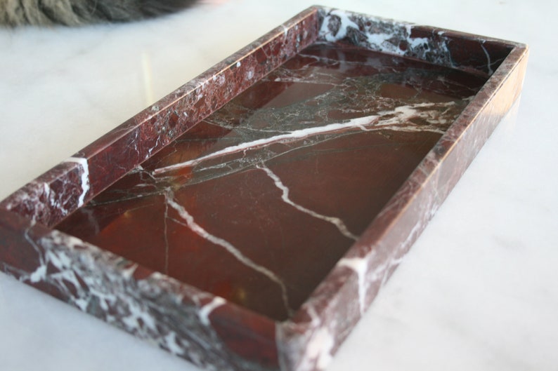 May include: A rectangular red marble tray with white veining. The tray has a smooth, polished surface and a raised rim.