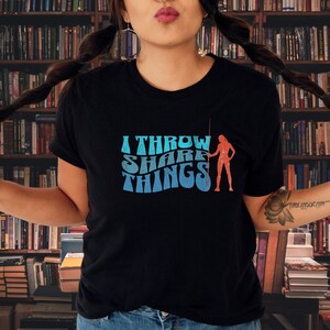 May include: A black t-shirt with a blue and red graphic that says "I Throw Shade Things" and features a silhouette of a woman throwing a spear.