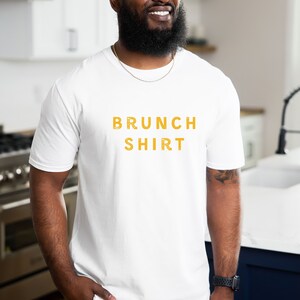 K&ouml;nnte beinhalten: Wei&szlig;es T-Shirt mit dem Aufdruck "BRUNCH SHIRT" in Gelb.