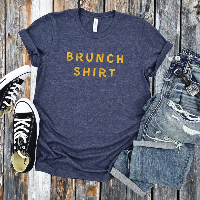 K&ouml;nnte beinhalten: Ein marineblaues T-Shirt mit dem Text "BRUNCH SHIRT" in Gelb.
