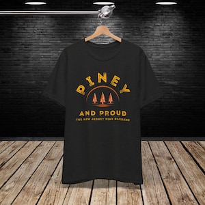 May include: Black t-shirt with a yellow and orange graphic design that says "Piney and Proud The New Jersey Pine Barrens".