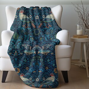 May include: A blue and green throw blanket with a repeating pattern of stylized birds and floral designs. The blanket features a dark blue background with green leaves and flowers.