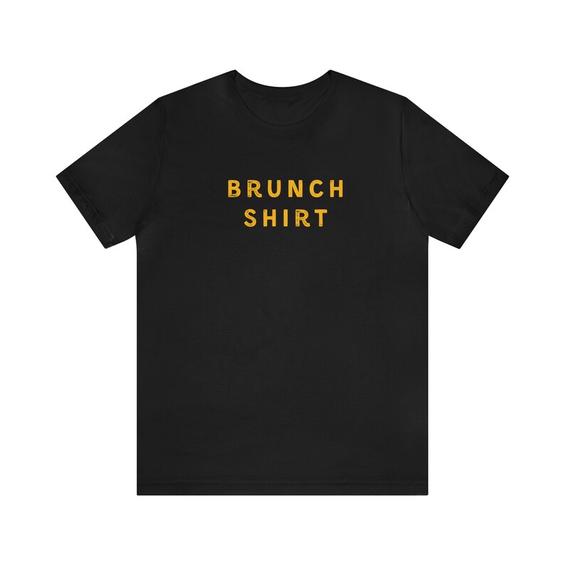 K&ouml;nnte beinhalten: Schwarzes T-Shirt mit dem Text "BRUNCH SHIRT" in Gelb.