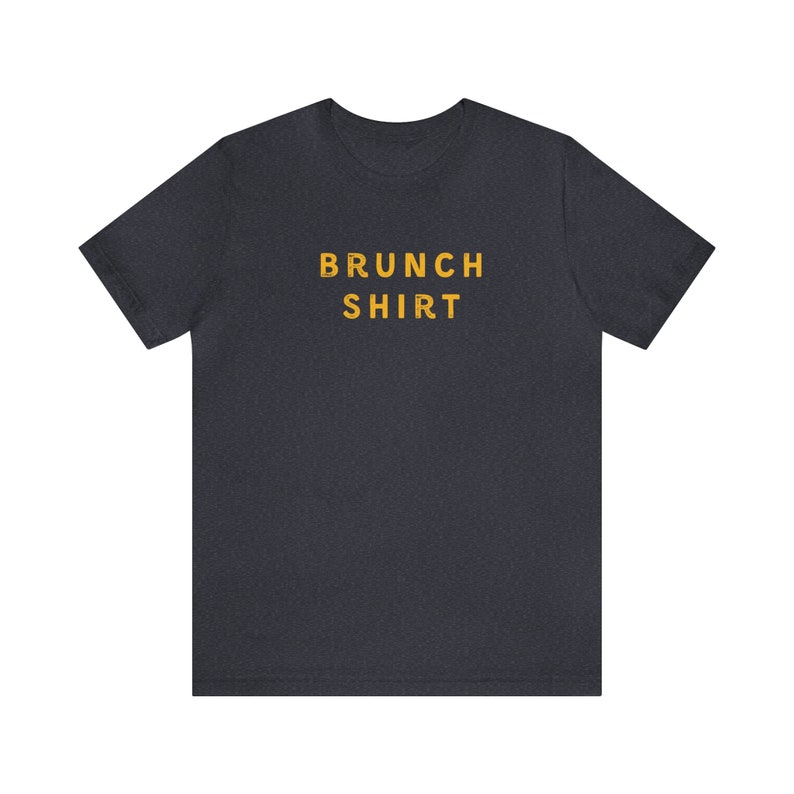 K&ouml;nnte beinhalten: Ein dunkelgraues T-Shirt mit dem Aufdruck "BRUNCH SHIRT" in Gelb.