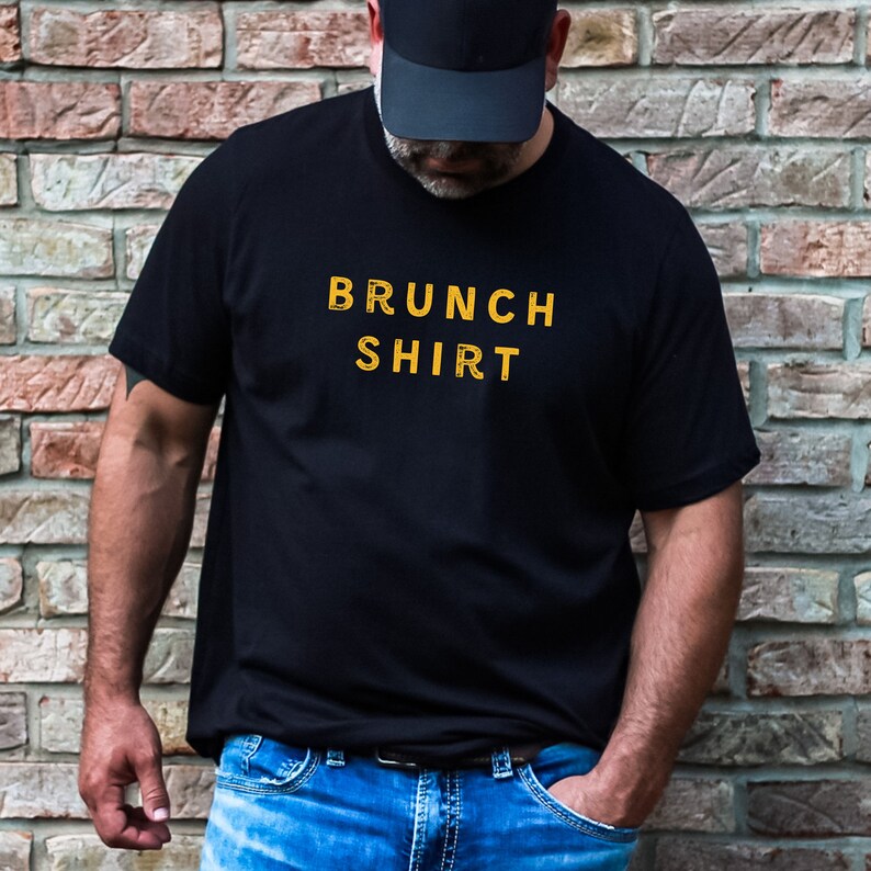 K&ouml;nnte beinhalten: Ein schwarzes T-Shirt mit dem Aufdruck "BRUNCH SHIRT" in Gelb.