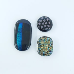 May include: Three glass cabochons with iridescent finishes. One is black with a blue stripe, one is black with white polka dots, and one is black with gold and blue stripes.