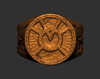 May include: A gold-colored ring with a circular design featuring a stylized V inside a circle with radiating lines. The ring has a textured surface.