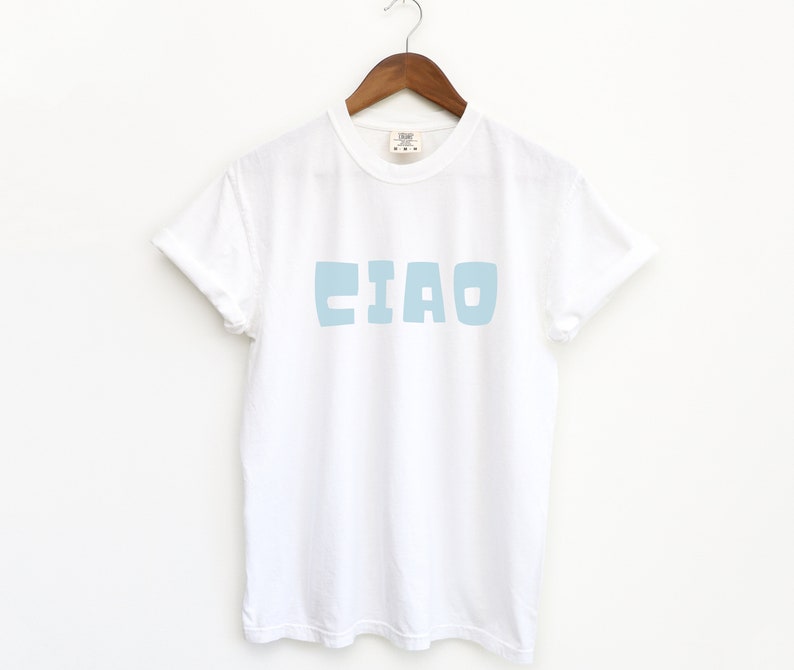 May include: White t-shirt with a light blue "CIAO" graphic printed on the front.