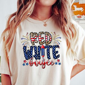 May include: A white t-shirt with a red, white, and blue graphic that says "Red White Boojee" with fireworks and a rocket.
