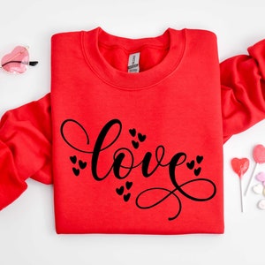 May include: Red sweatshirt with the word "love" written in black cursive script with small hearts surrounding the word.
