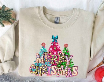 May include: A beige sweatshirt with a festive design featuring three Christmas trees and the words "Merry Christmas" in colorful, glittery letters.